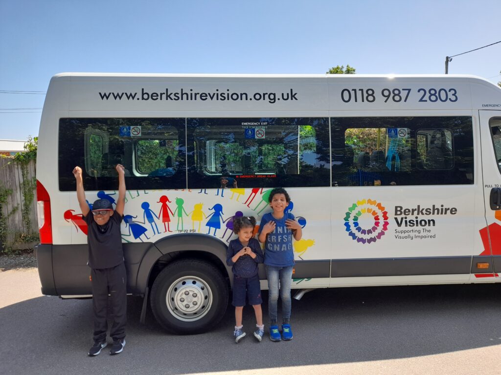 The Berkshire Vision Children's minibus. 3 children are stood next to it and smiling