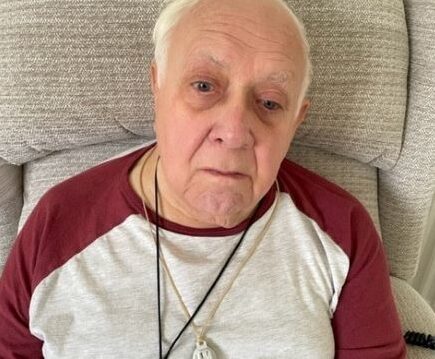 Mike sat in an armchair he is wearing a red and white top and has short white hair.