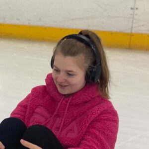 Dayzie is on a sldge on an ice rink she is wearing a pink hoodie and headphones.