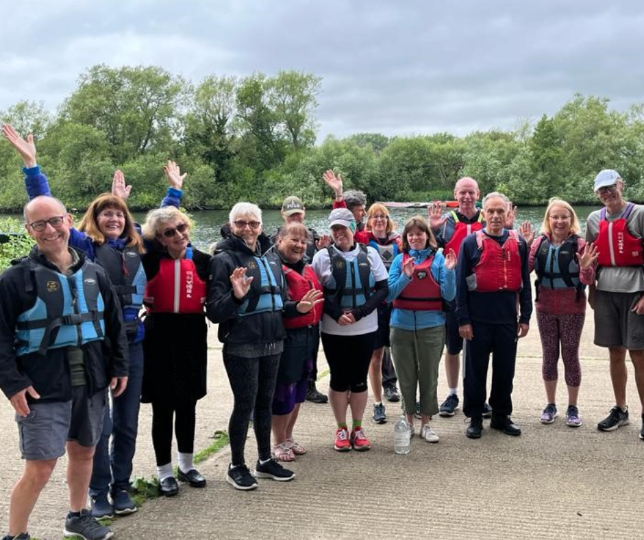 a group of people smiling with their arms in the air, wearing lifejackets ready to go canoeing.