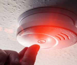 a smoke alarm being pressed to test it. the red light on it is flashing