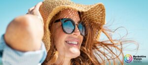 a photo of a woman wearing sunglasses and a straw hat. The sky behind her is blue
