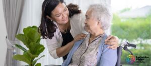 A photo of an older lady in a wheelchair being talked to kindly by a younger person