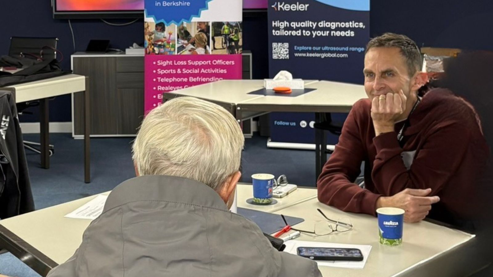 A photo of phil smiling while helping a berkshire vision member with their phone