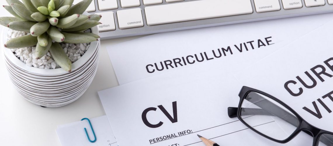 A white computer keyboard, with a paper CV in front of it. Glasses and a plant are next to it