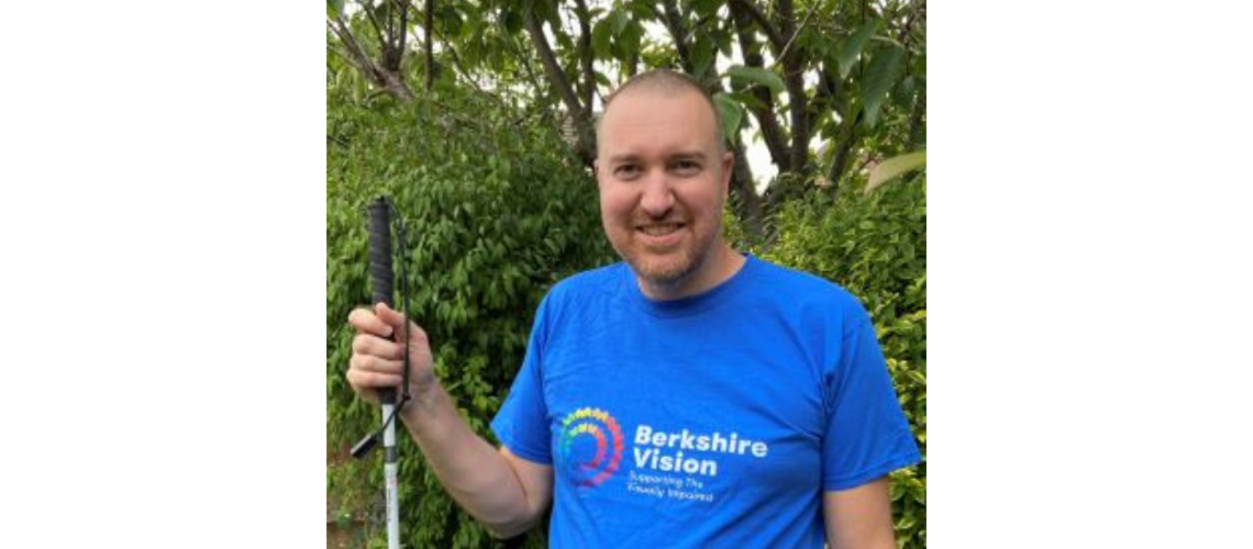 Chris is wearing a blue berkshire vision t-shirt and is holding his white cane