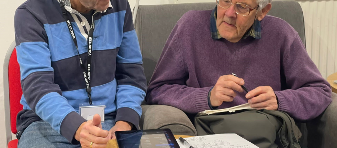 a volunteer is helping an older gentlemen to use an ipad