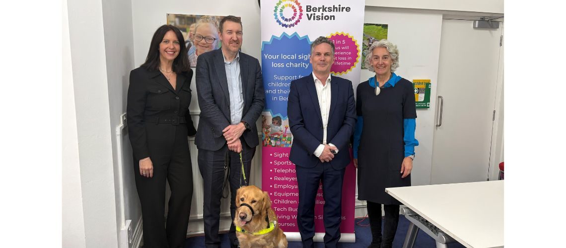 Berkshire Vision trustees Clare, Chris, Gavin and chair of trustees Jane stood in front of a berkshire vision pull up. Chester, Chris' guide dog is at the front