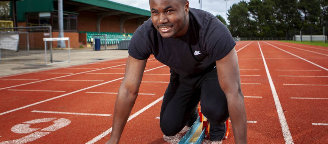 A photo of Soul on a running track. He is in crouched in starting position ready to run. He is wearing a black tracksuit.